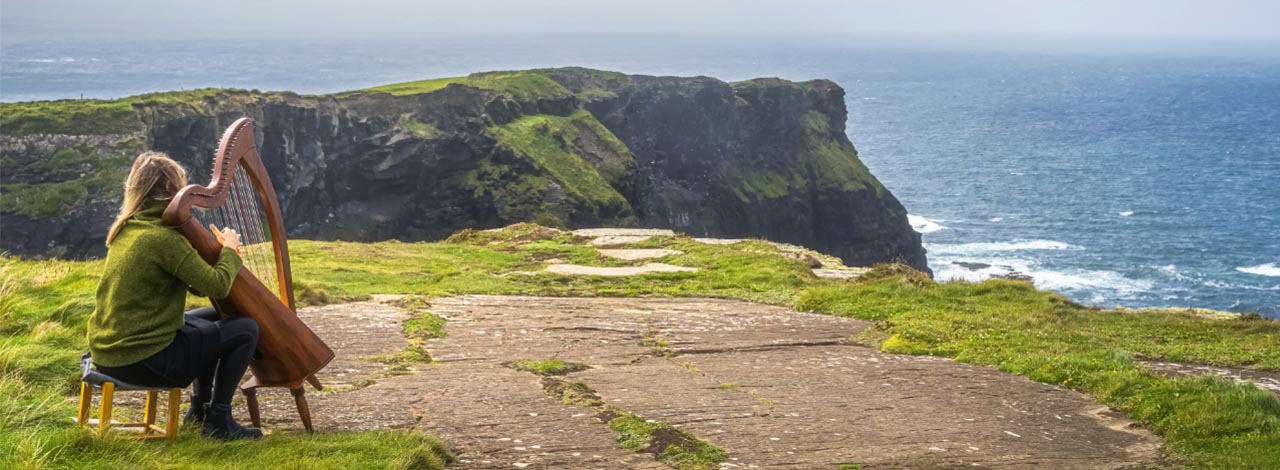Ireland, woman playing a harp near the sea – header Ireland, woman playing a harp near the sea
