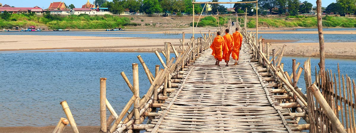 3 orange-robed monks crossing the Mekong on a bamboo bridge